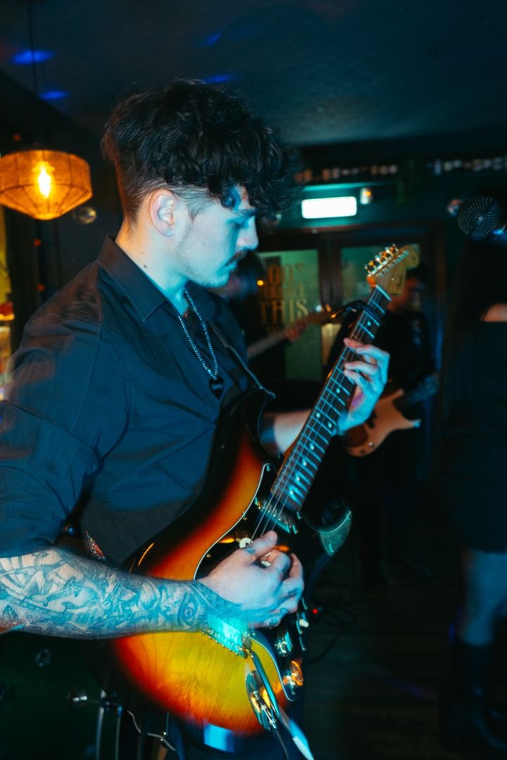 Close-up of Jack mid-song, tattooed forearm across a sunburst guitar, lit in blue and amber