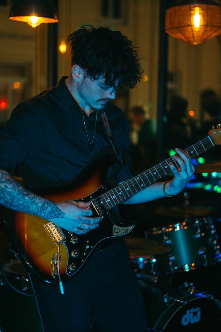 Jack playing a sunburst electric guitar on stage under warm hanging lamps